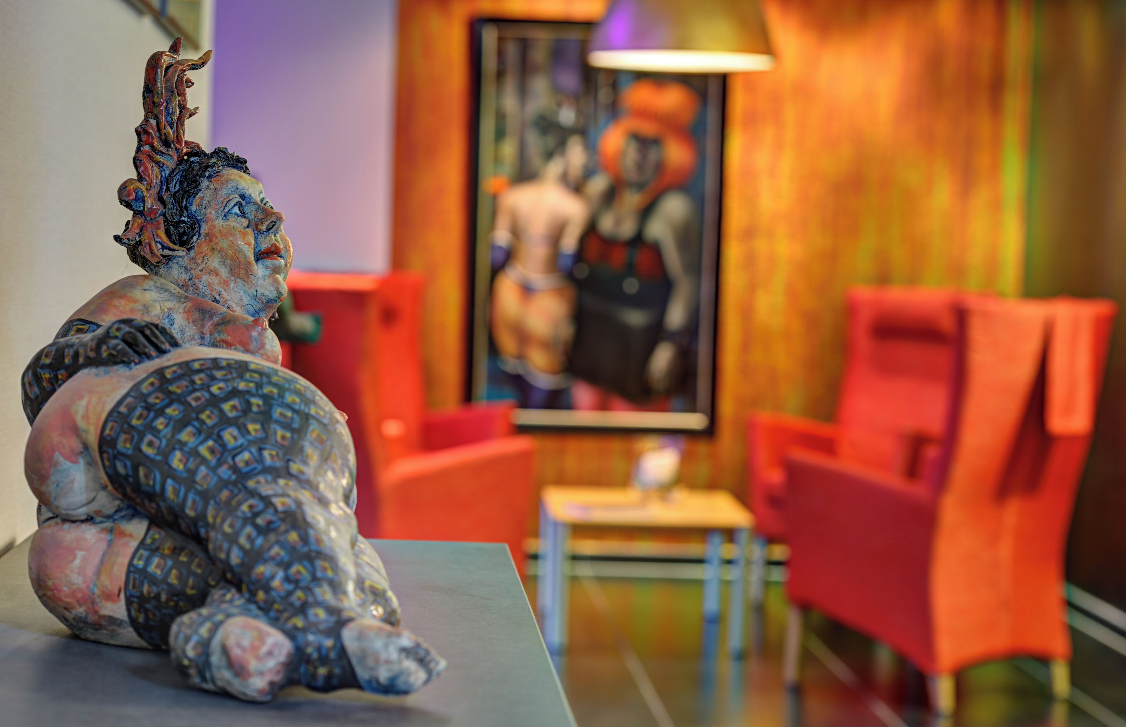 A statue on a table, red chairs, and a painting in a room.