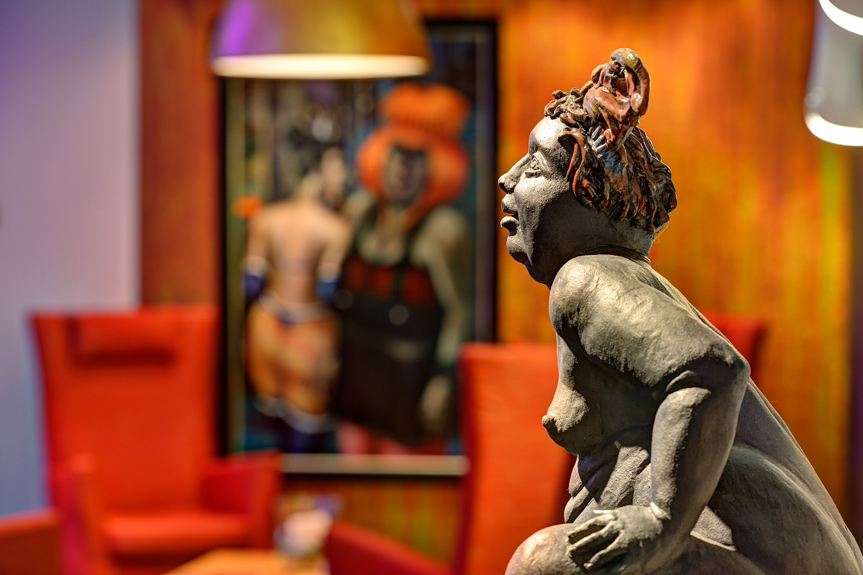Una escultura en una habitación con una silla roja y un cuadro al fondo.