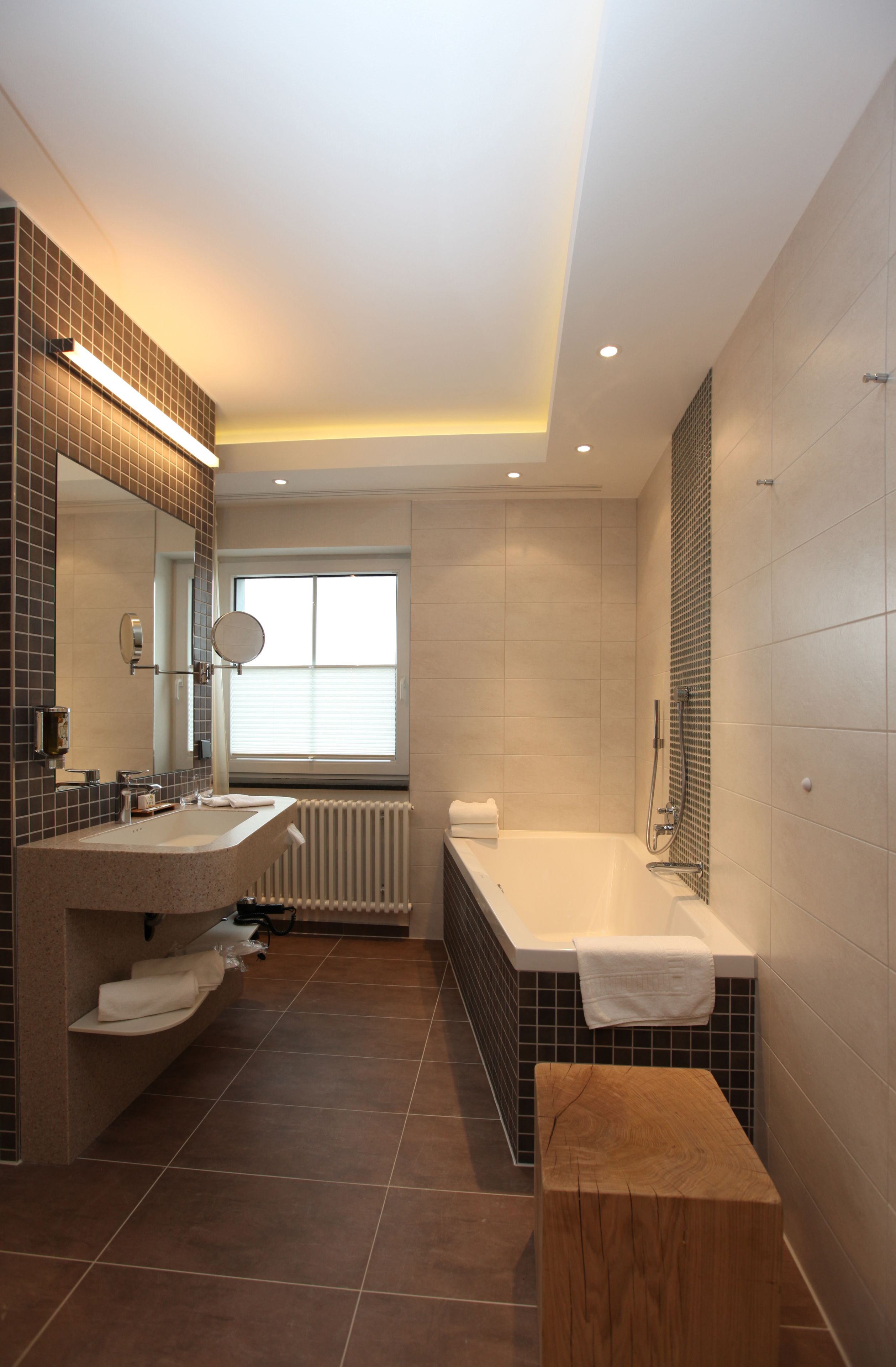 Un baño moderno con un espejo grande, dos lavamanos, una bañera y un ventanal que proporciona luz natural.
