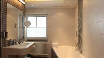 Un baño moderno con un espejo grande, dos lavamanos, una bañera y un ventanal que proporciona luz natural.