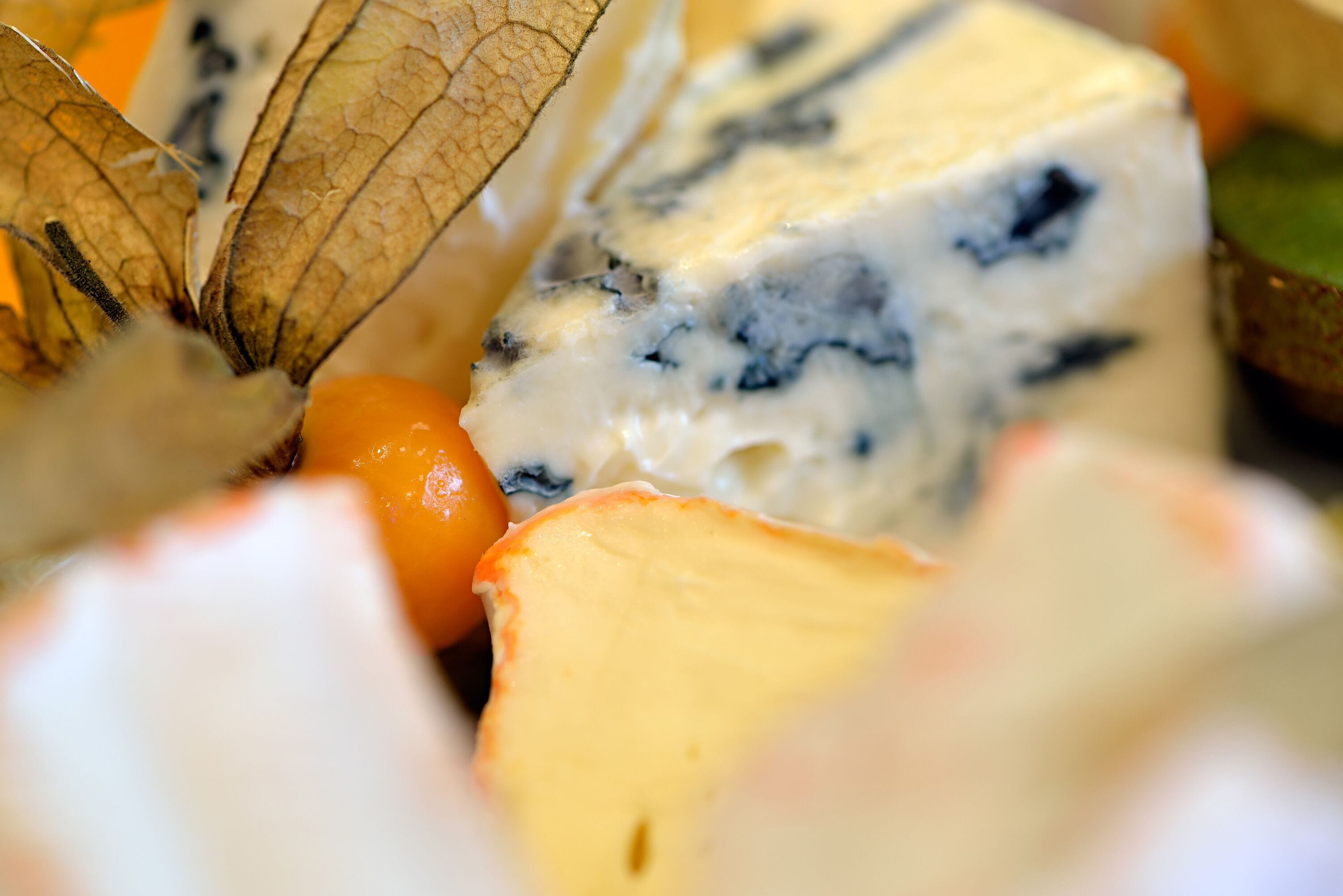 A close-up of a cheese platter with various cheeses and dried leaves.