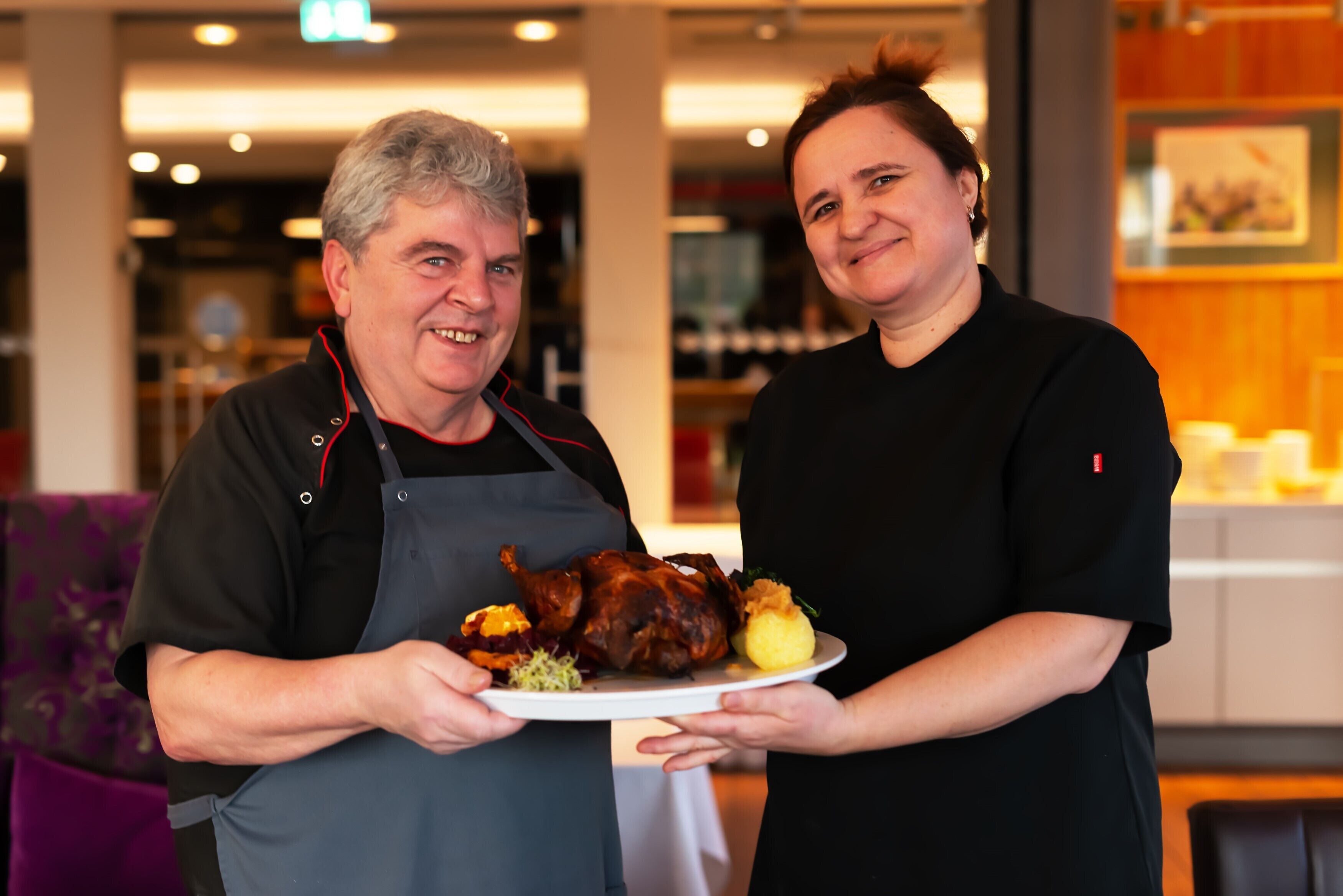 Twee personen houden een bord vast met geroosterd vlees en groenten.