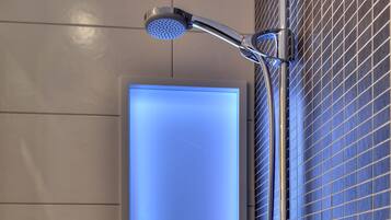 A modern bathroom with a glass-enclosed shower, a handheld showerhead, and a wall-mounted faucet.