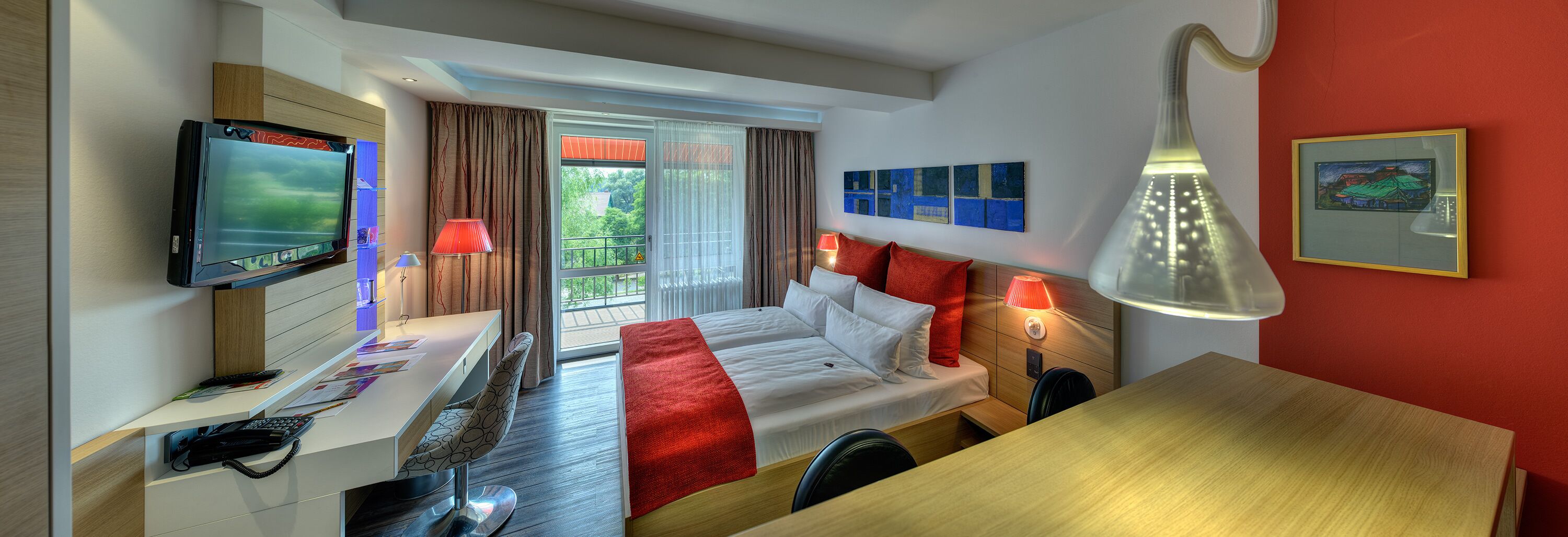 A hotel room with a bed, desk, TV, and a balcony with curtains.