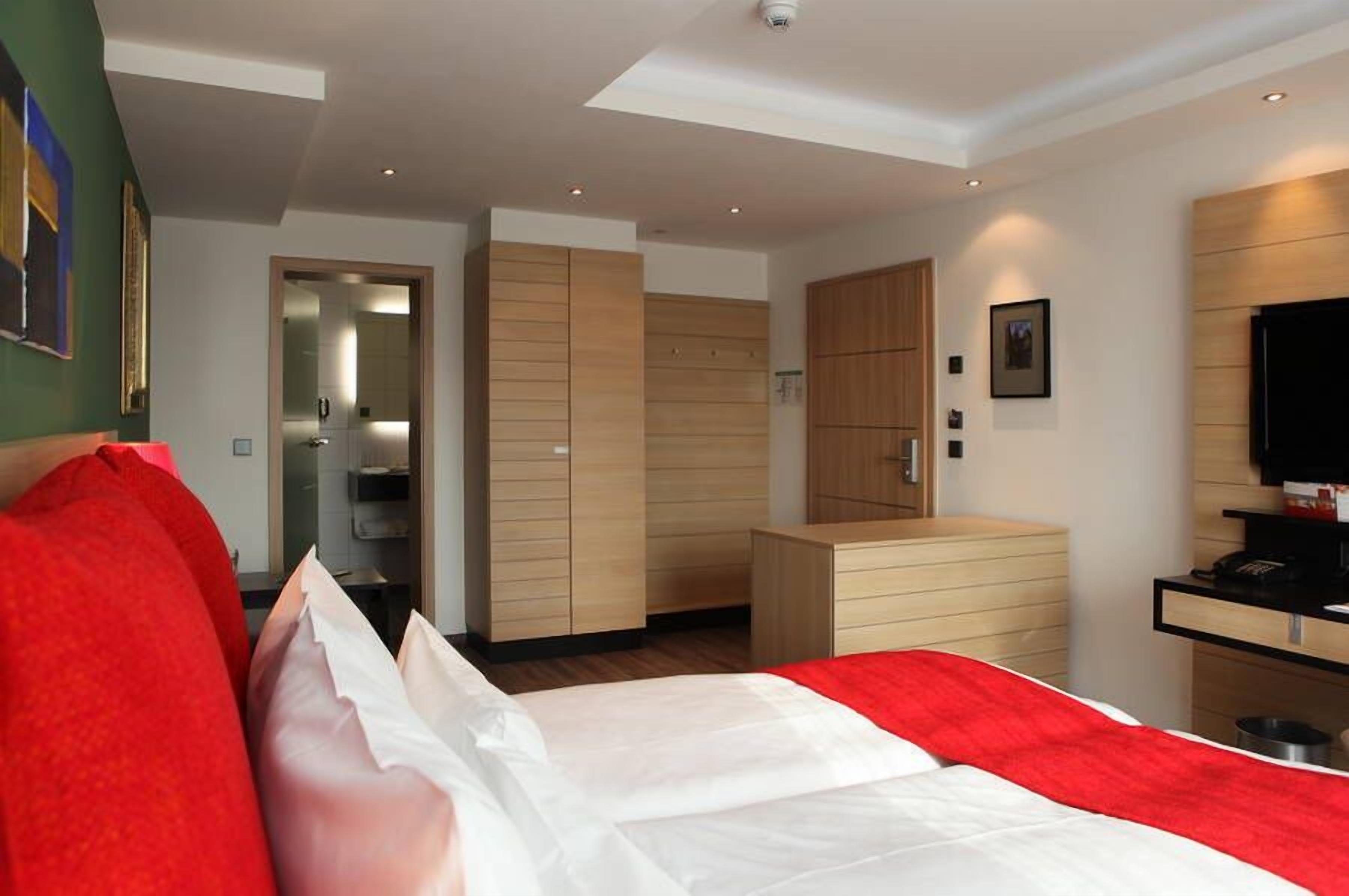 A modern hotel room with a bed, a desk, and built-in wardrobes.