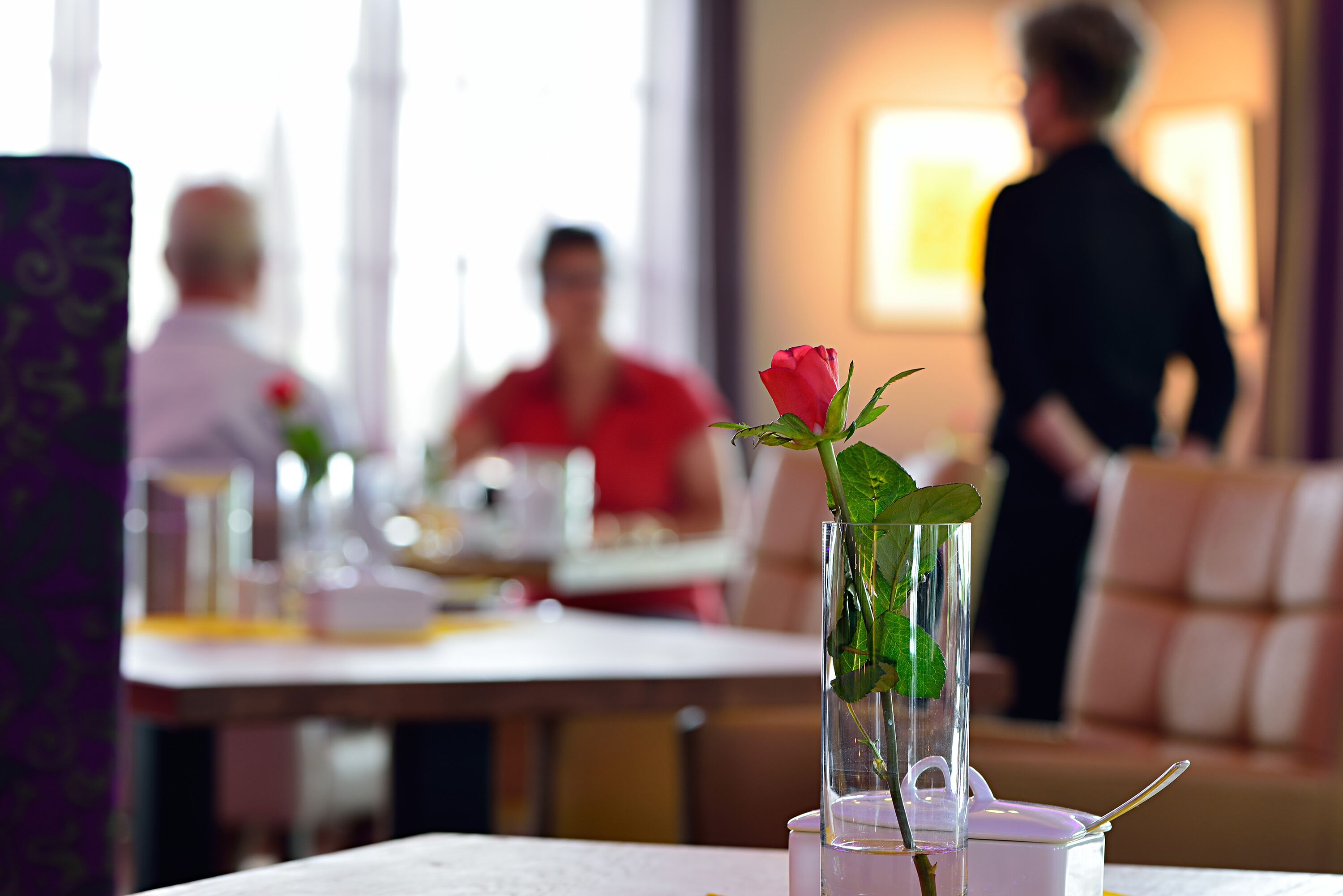 A dining table with a clear glass vase containing a single rose.