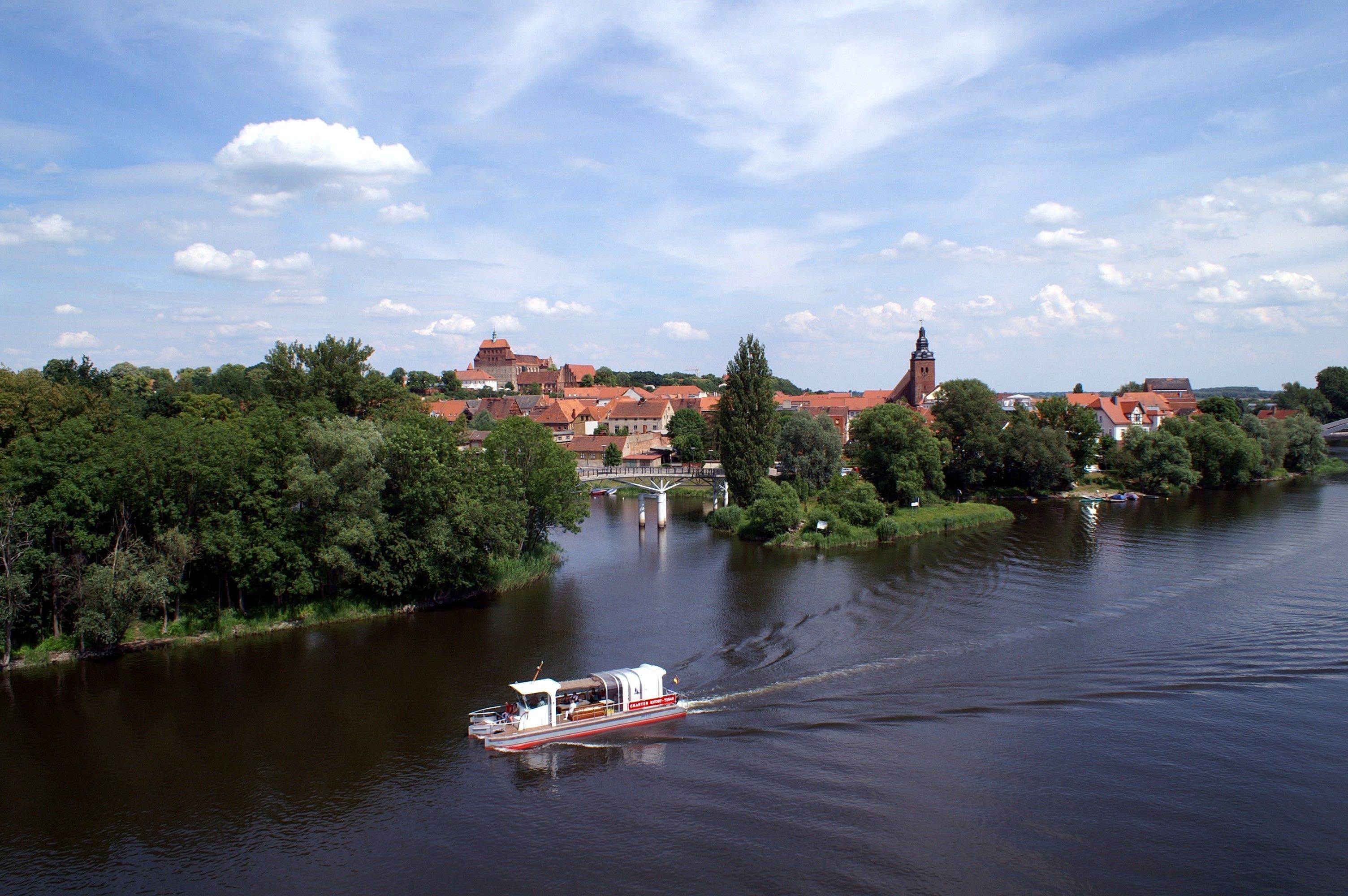 A river with a boat, surrounded by greenery and buildings with red roofs.