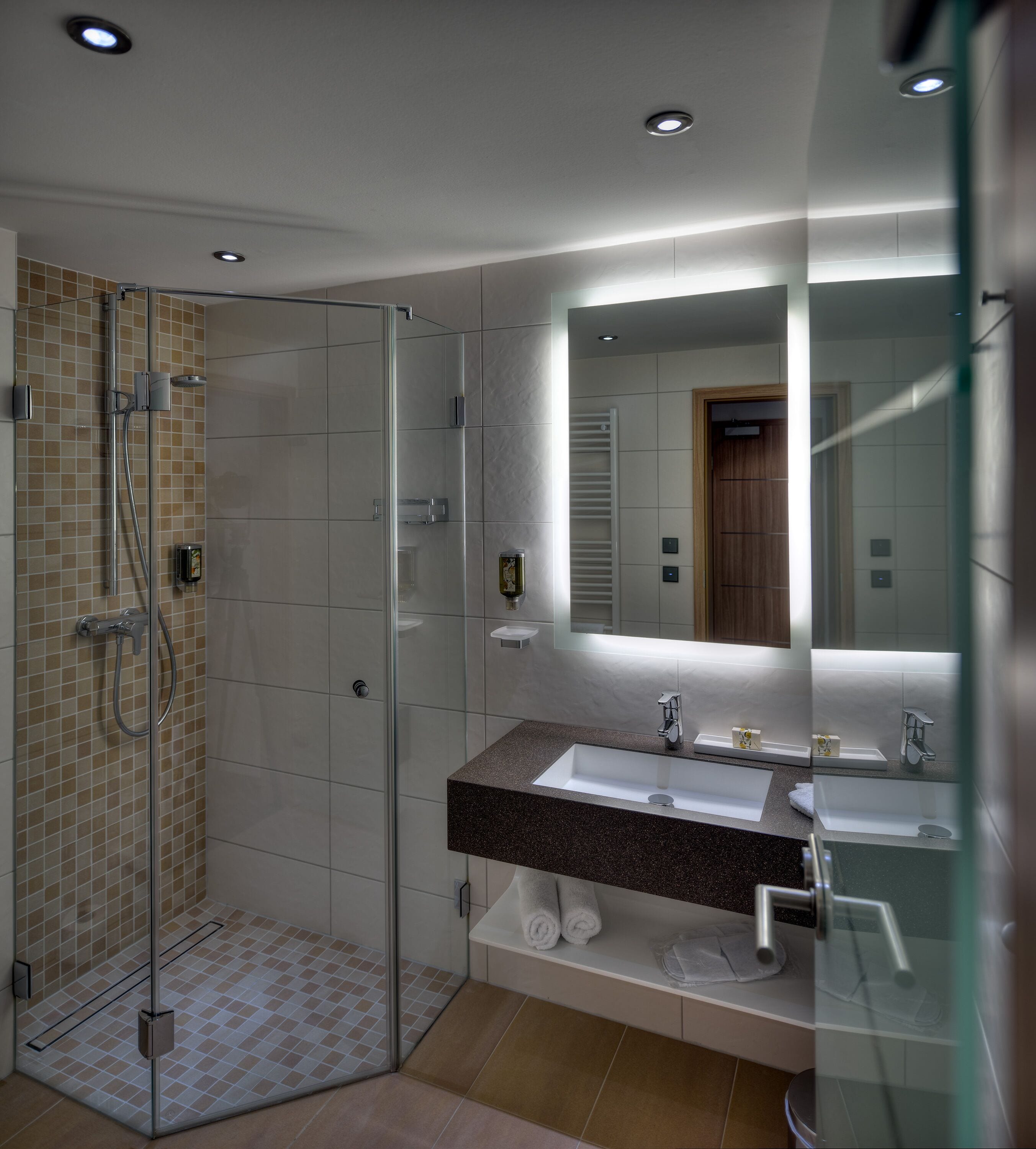 Un baño moderno con ducha de vidrio, lavamanos de mármol y un espejo grande.