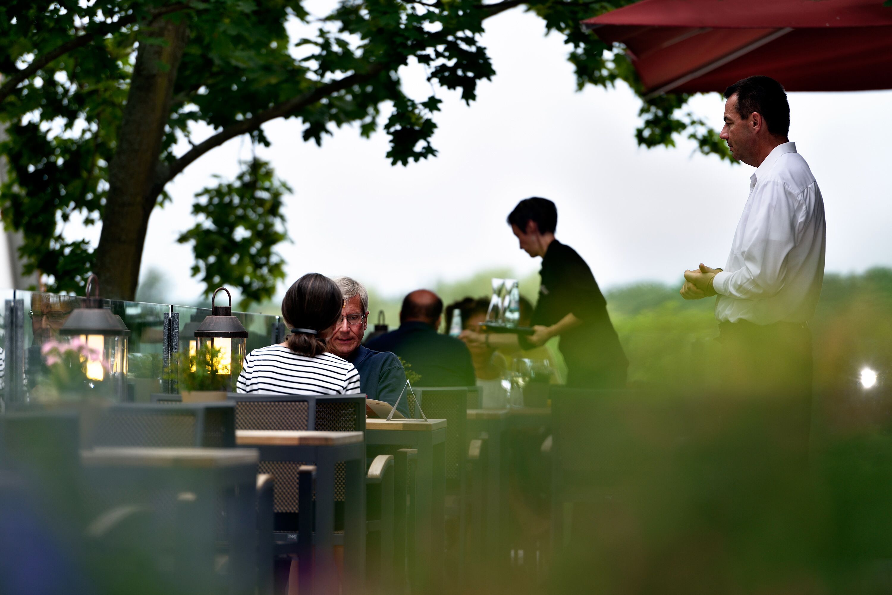 An outdoor dining area with tables and chairs, surrounded by trees and a red canopy.