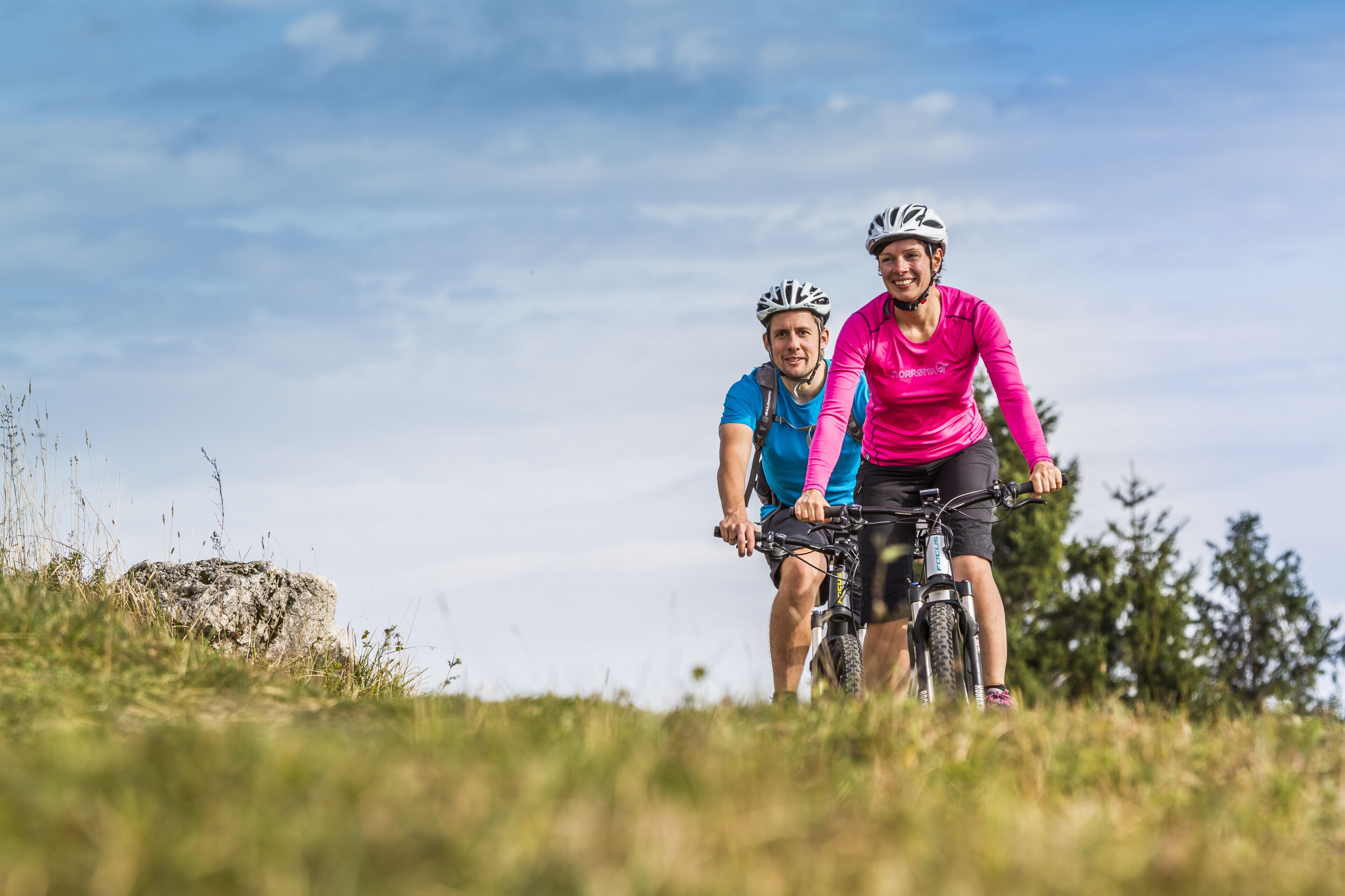Deux personnes à vélo, dans un environnement extérieur verdoyant.