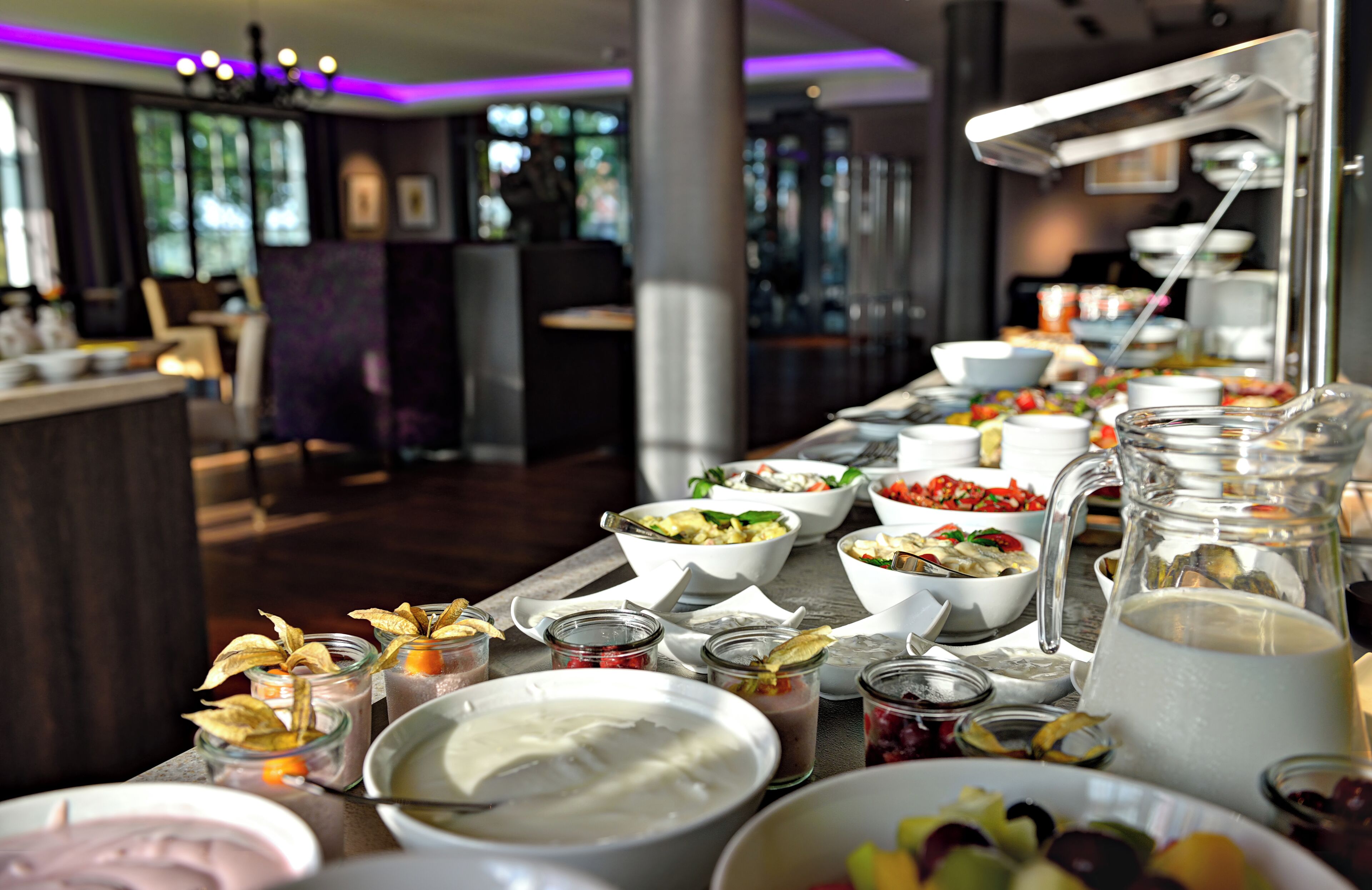 A buffet setup with various food items and beverages, including bowls of salad, fruit, and a pitcher of water.