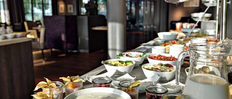 Una mesa de buffet con diversos alimentos y bebidas, como ensaladas, fruta y una jarra de agua.