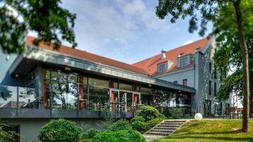 A modern building with a glass facade, a red roof, and a well-maintained garden with a pathway leading to the entrance.