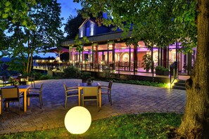 Un área de comedor al aire libre con mesas y sillas, un gran globo iluminado y un edificio con paredes de vidrio e iluminación morada.