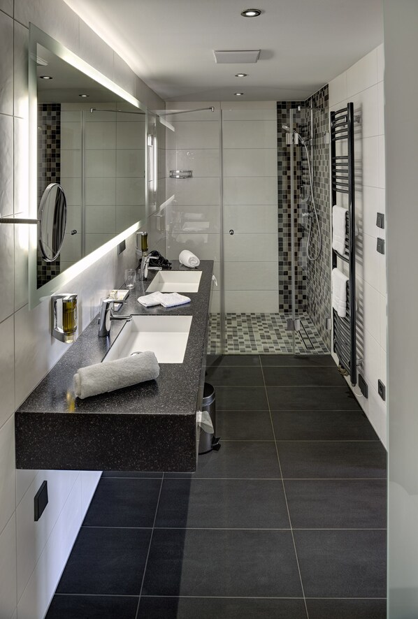 Un baño moderno con un espejo grande, dos lavabos, zona de ducha y un perchero para toallas.