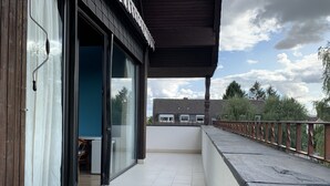 Un balcón con barandilla de madera, puerta de vidrio y vista a una zona residencial.