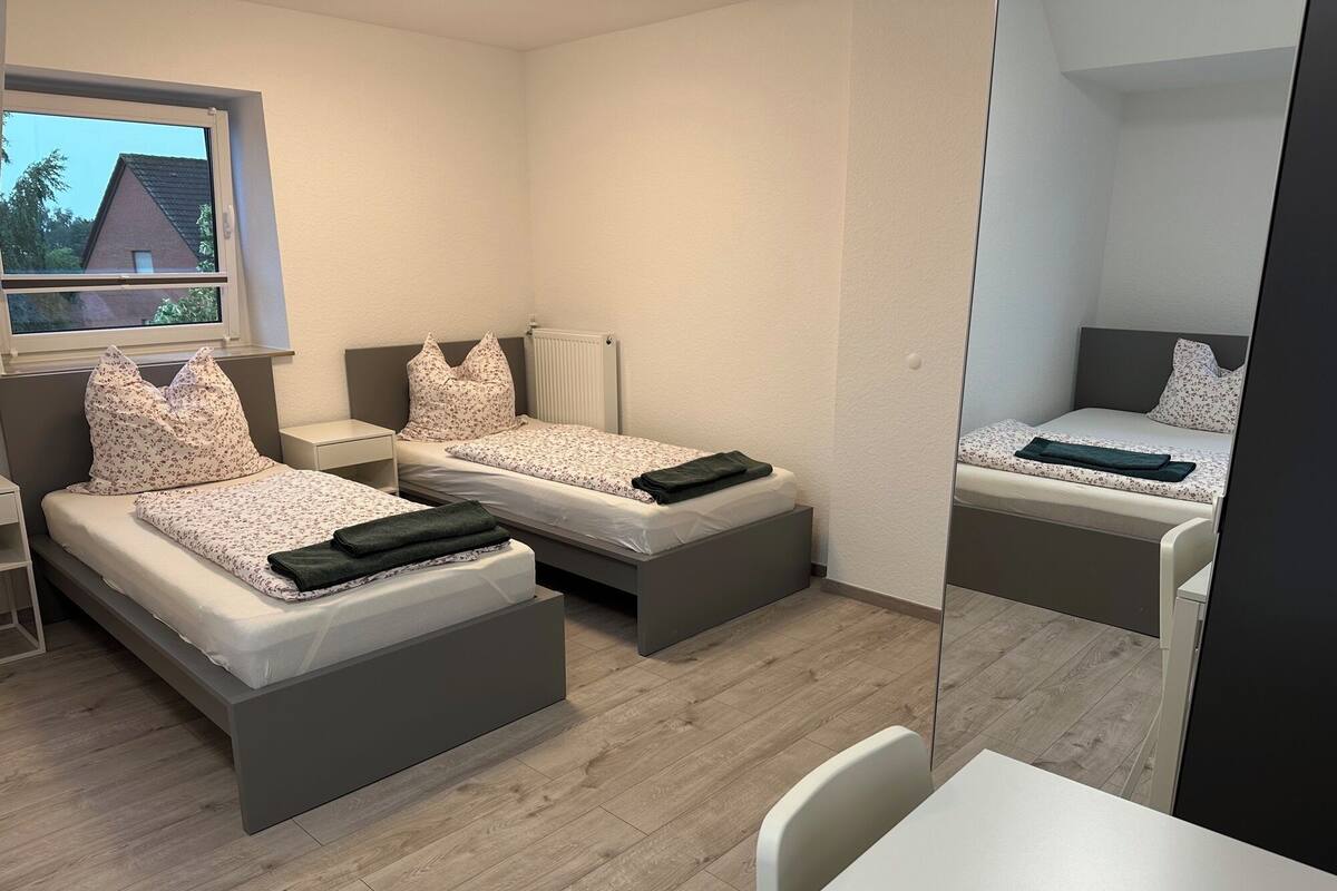 A modern bedroom with two beds, a small table, and a chair.