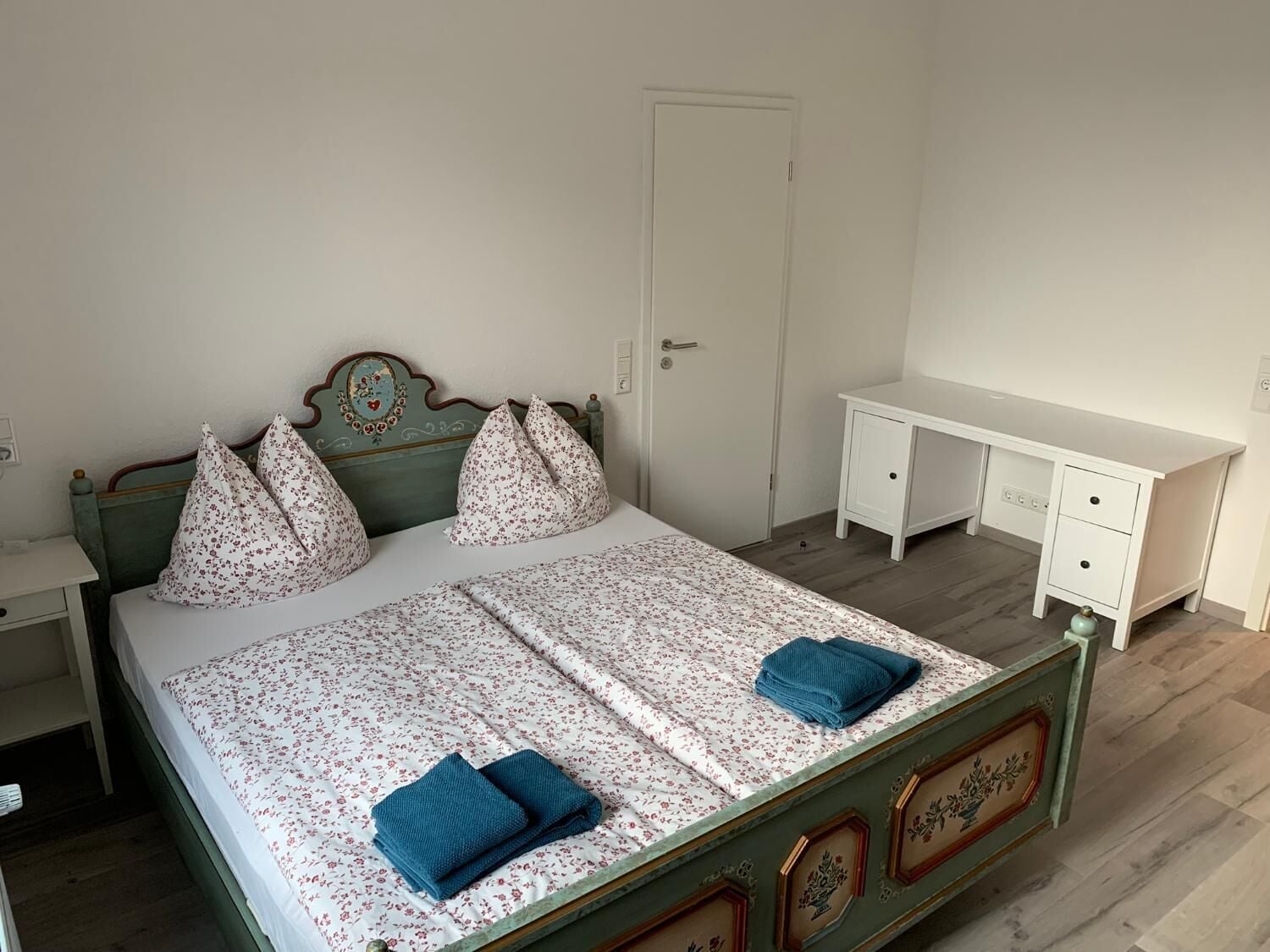 Ein Schlafzimmer mit Bett, Nachttisch, Kommode und Tür.