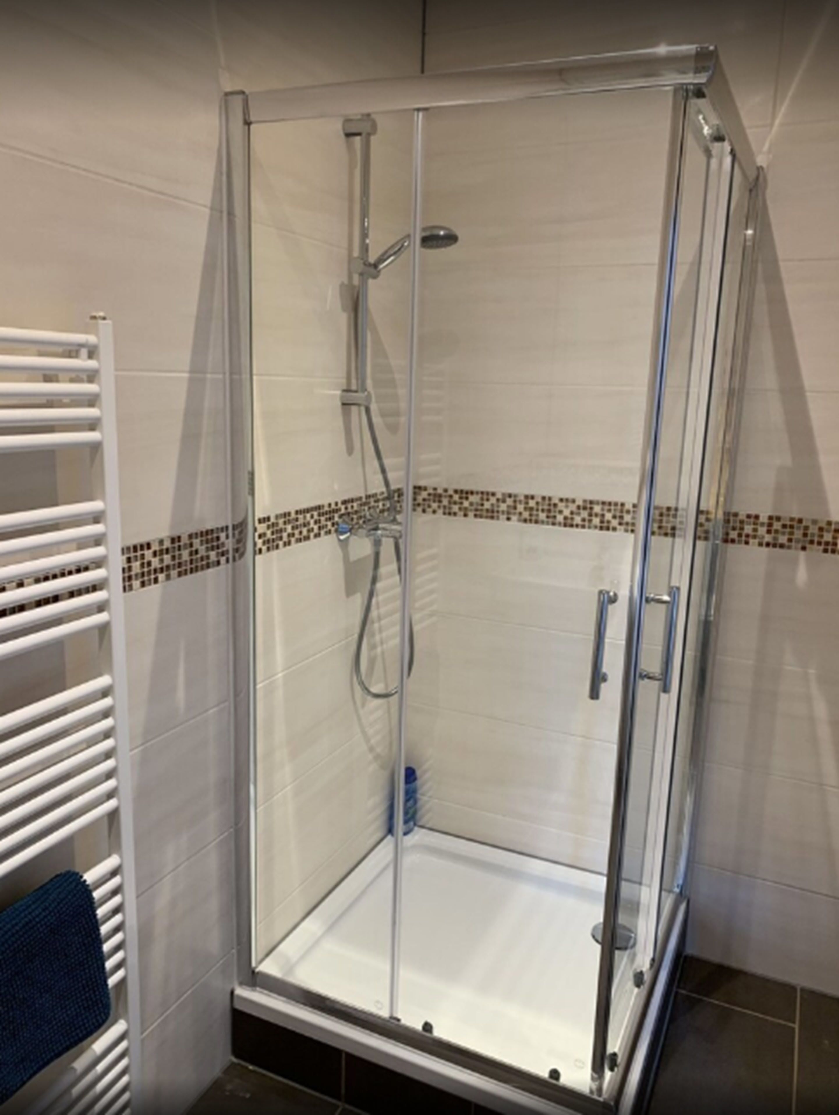Un box de ducha con paredes de vidrio, suelo de azulejos y un toallero blanco a la izquierda.