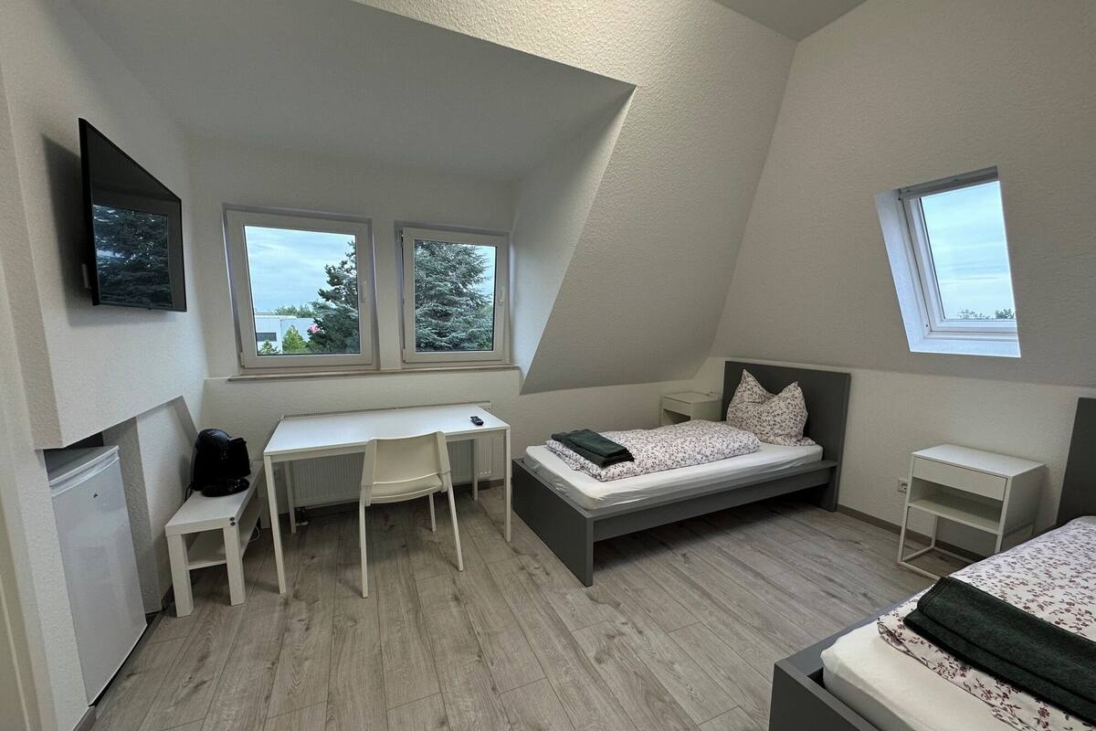 A bedroom with a bed, a desk, and two windows.