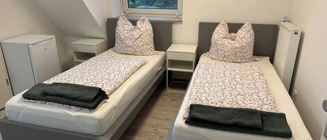 A twin room with two beds, a small desk, a radiator, and a window with a view of trees.