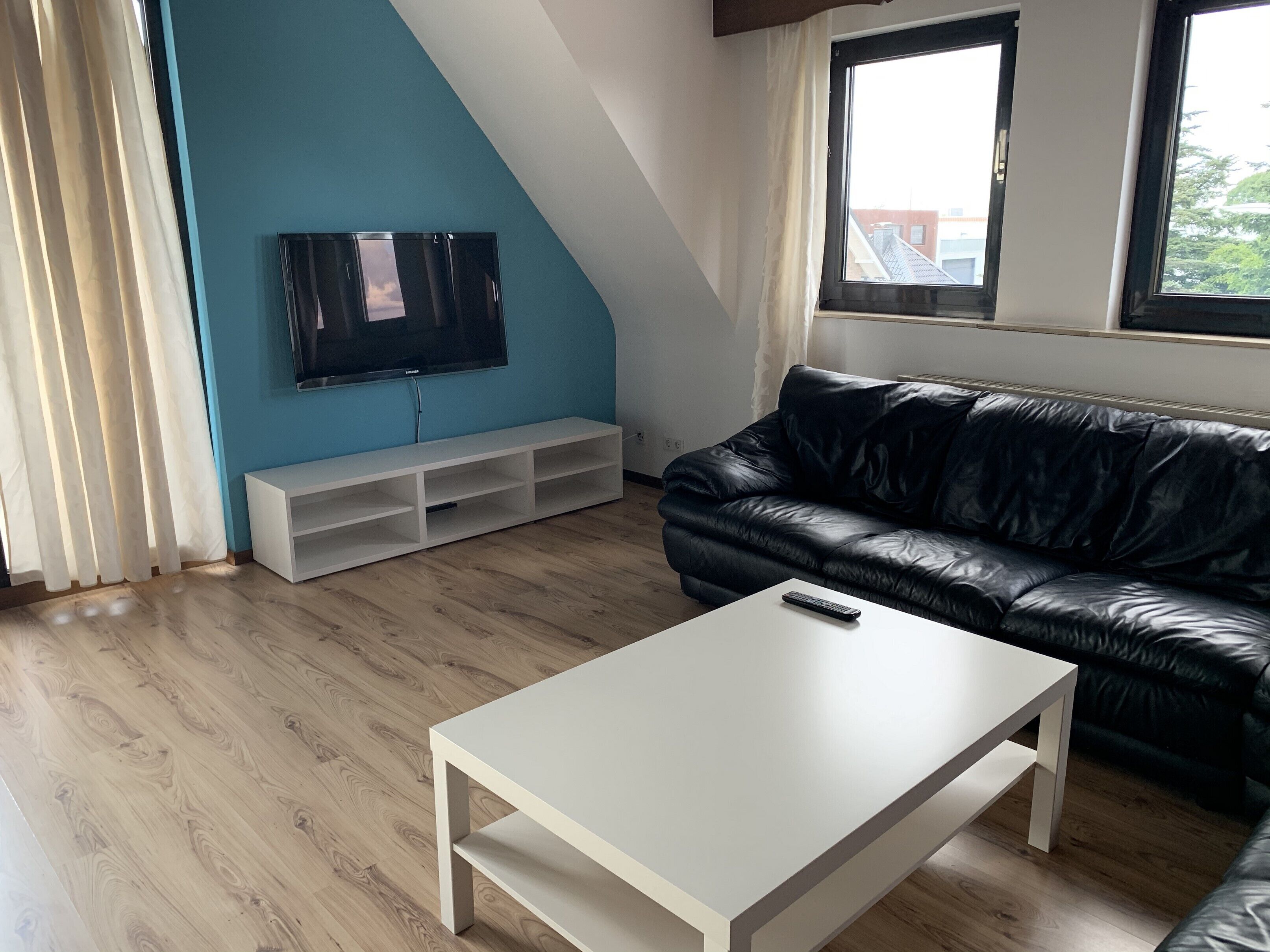 Un salon avec un téléviseur, un canapé en cuir noir, une table basse blanche et un plancher en bois.