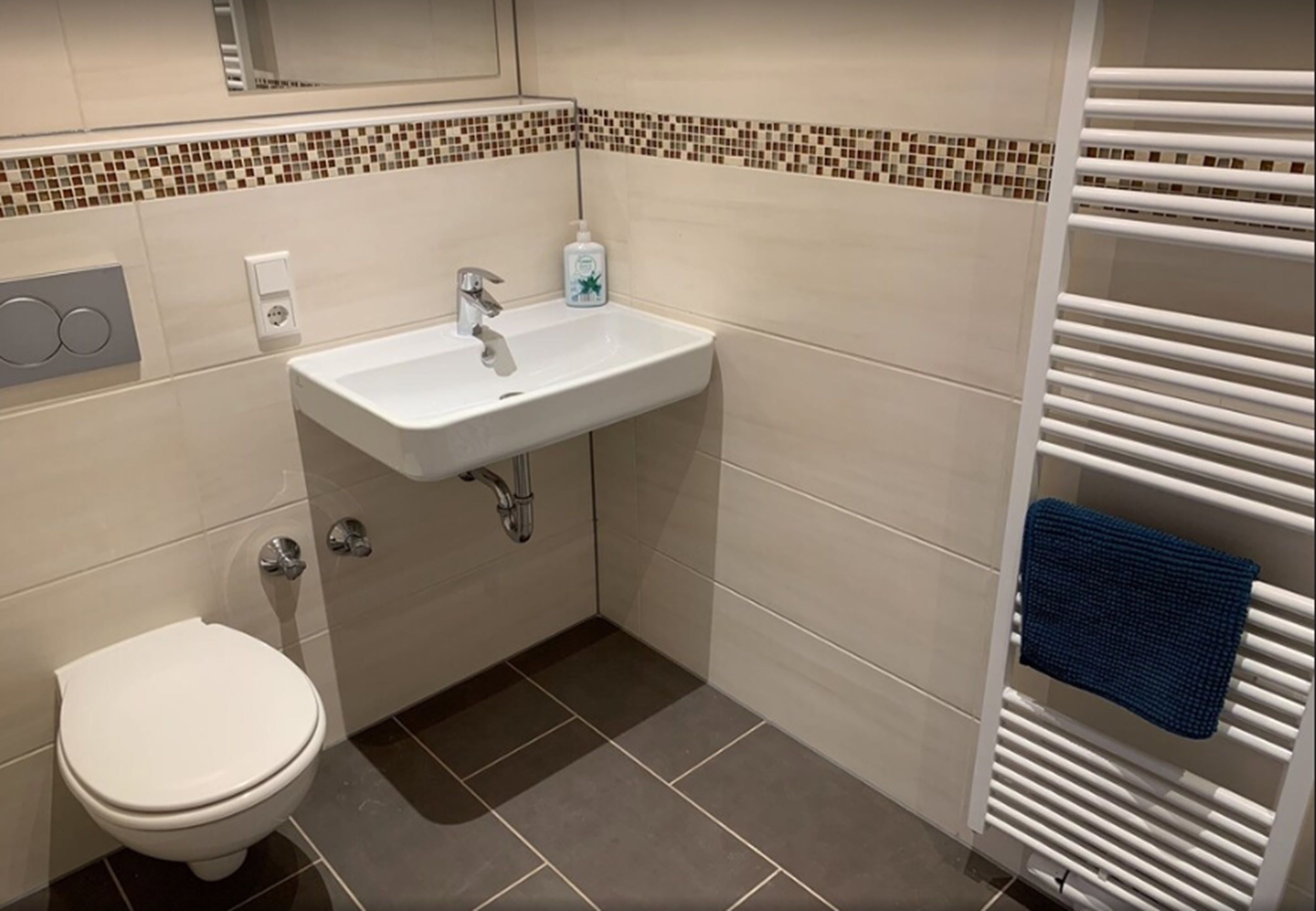 Un baño con un lavabo blanco, un inodoro y un perchero con una toalla azul.