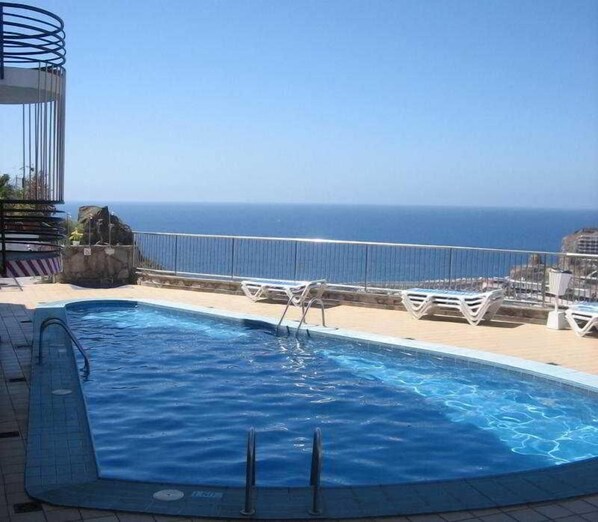 Una piscina al aire libre, sombrillas, sillones reclinables de piscina