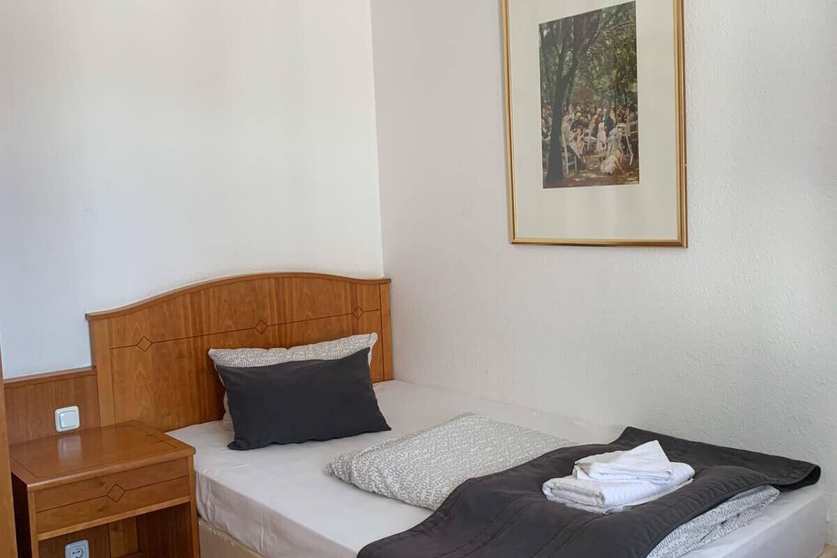 A single bed with a wooden headboard, a nightstand, a bedside table, and a framed picture on the wall.