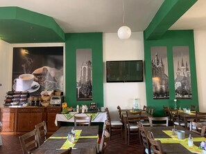 Un restaurante con paredes verdes, una amplia exhibición de café y varias mesas para comer.
