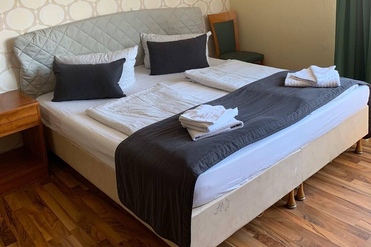 A neatly made bed with a quilted headboard, a wooden nightstand, and a green curtain.