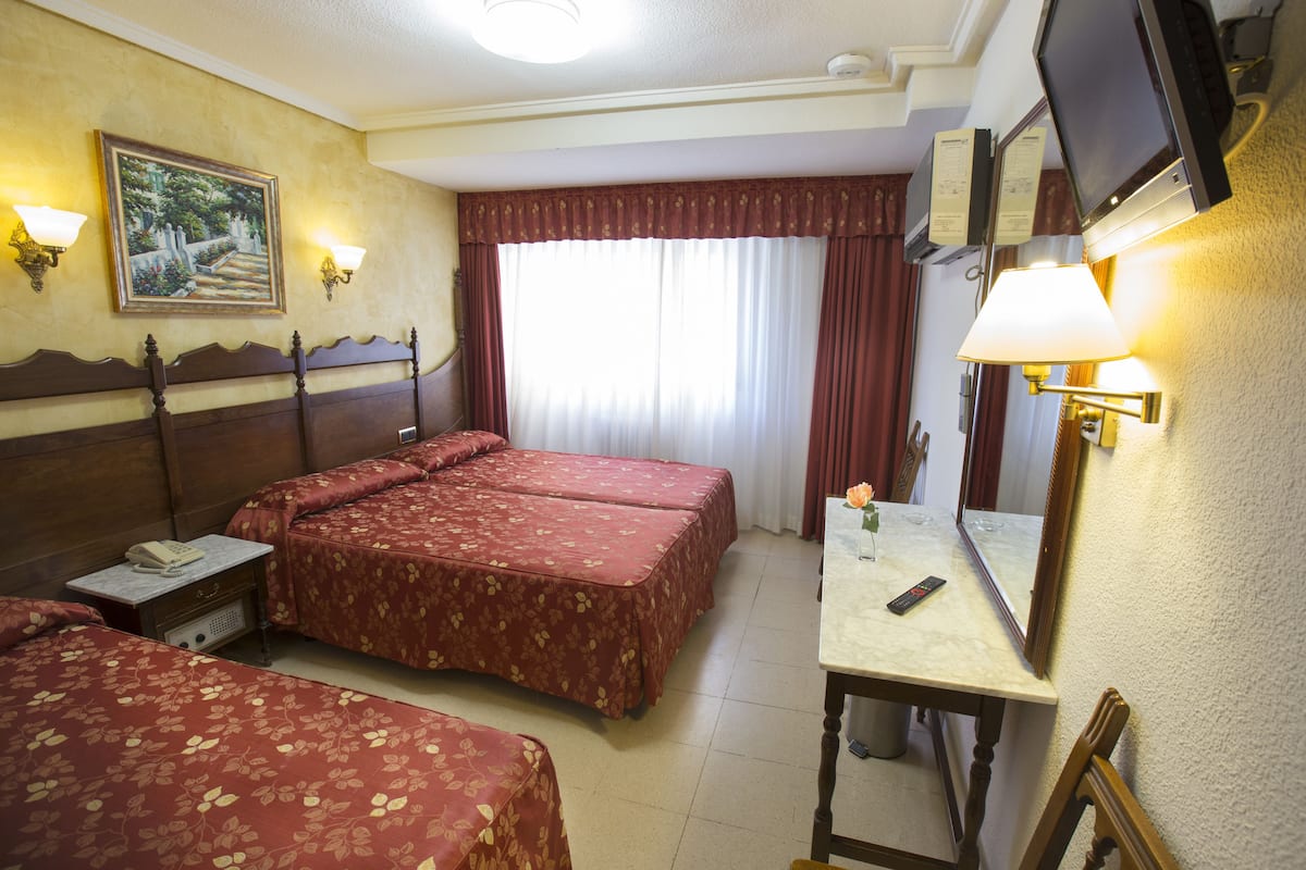 A hotel room with two beds, a desk, a chair, a TV, and a window with curtains.