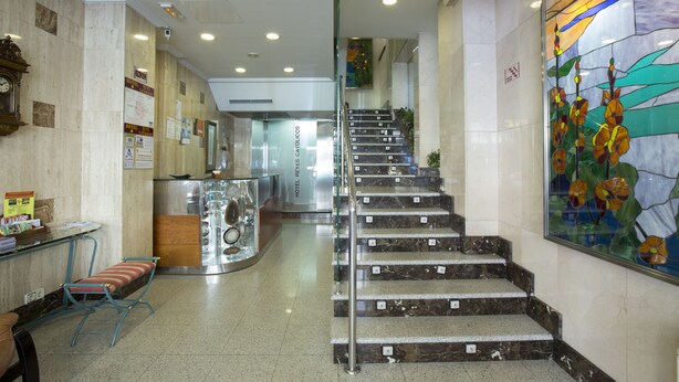 A hotel lobby with marble floors, a staircase, a reception desk, and a stained glass window. - Hotel Reyes Catolicos (Salamanca)
