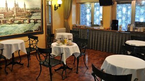 A dining area with tables set for breakfast, a painting of a cityscape on the wall, and a view of the river through the window. - Hotel Reyes Catolicos (Salamanca)