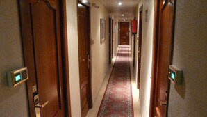 A hotel hallway with wooden doors, a red carpet, and a fire extinguisher on the wall. - Hotel Reyes Catolicos (Salamanca)