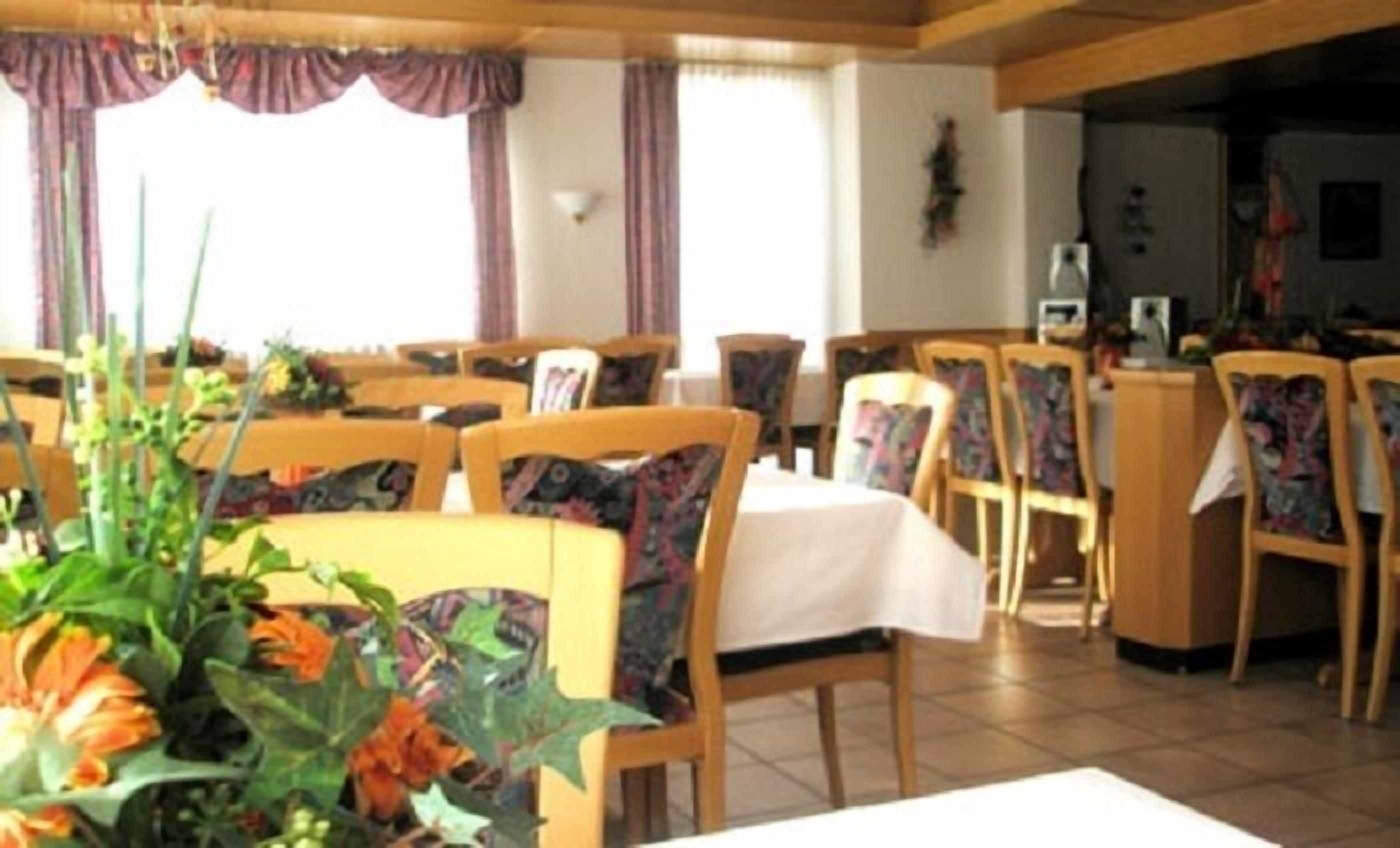 A dining area with wooden chairs and tables, a flower arrangement on the table, and a window with curtains.