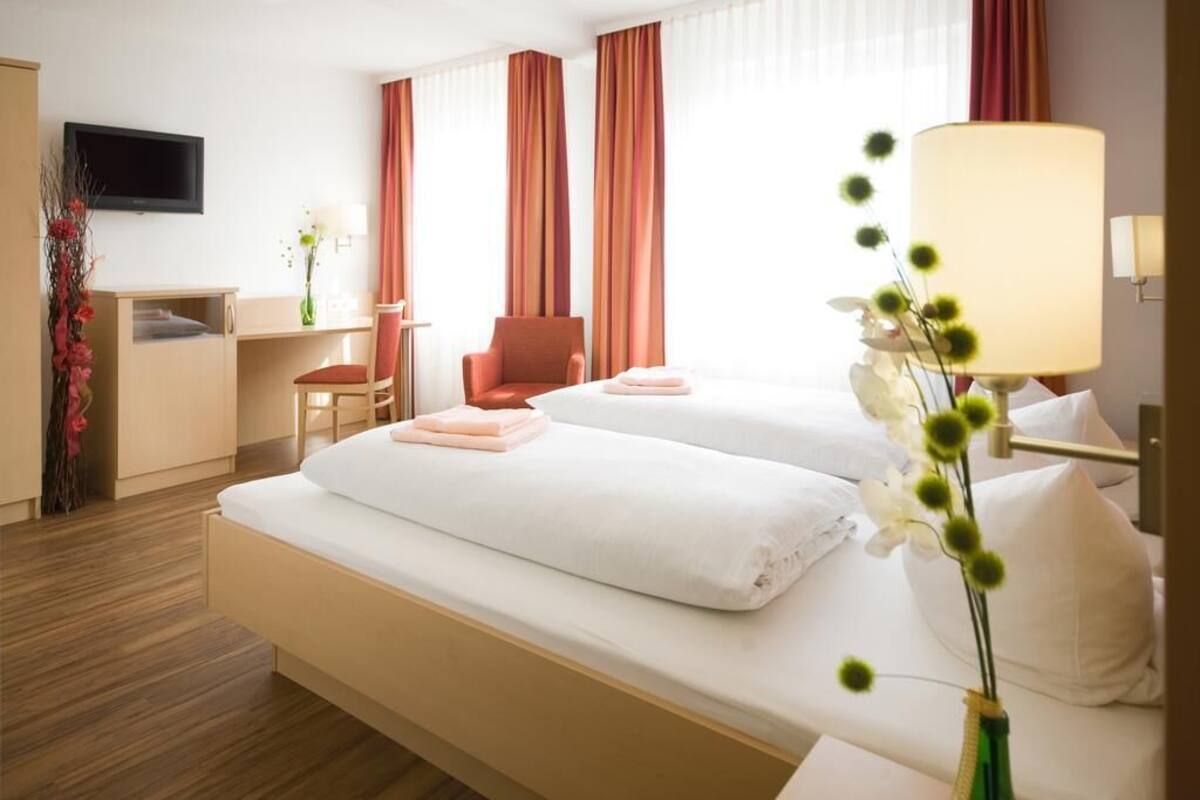 A hotel room with two beds, a desk, a chair, a TV, and a window with curtains.