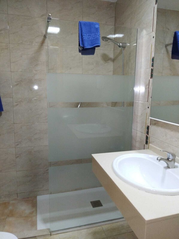 A modern bathroom with a glass-enclosed shower, a white sink, and a blue towel hanging on the wall.