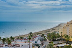 A coastal view with a beach, palm trees, and buildings. - Apartamentos Las Arenas (San Bartolomé de Tirajana)