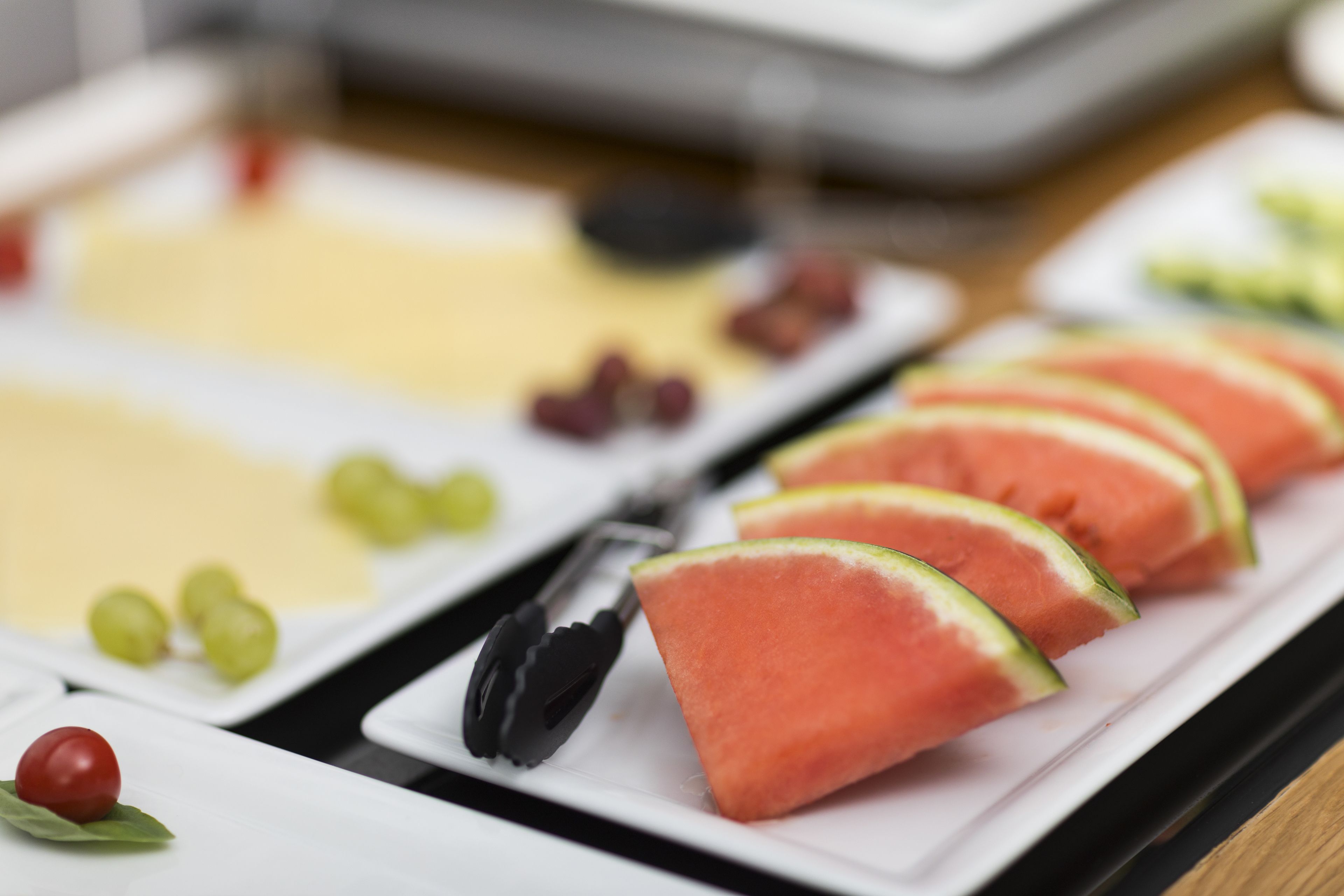 Una mesa de buffet con rebanadas de sandía, uvas y una selección de quesos.