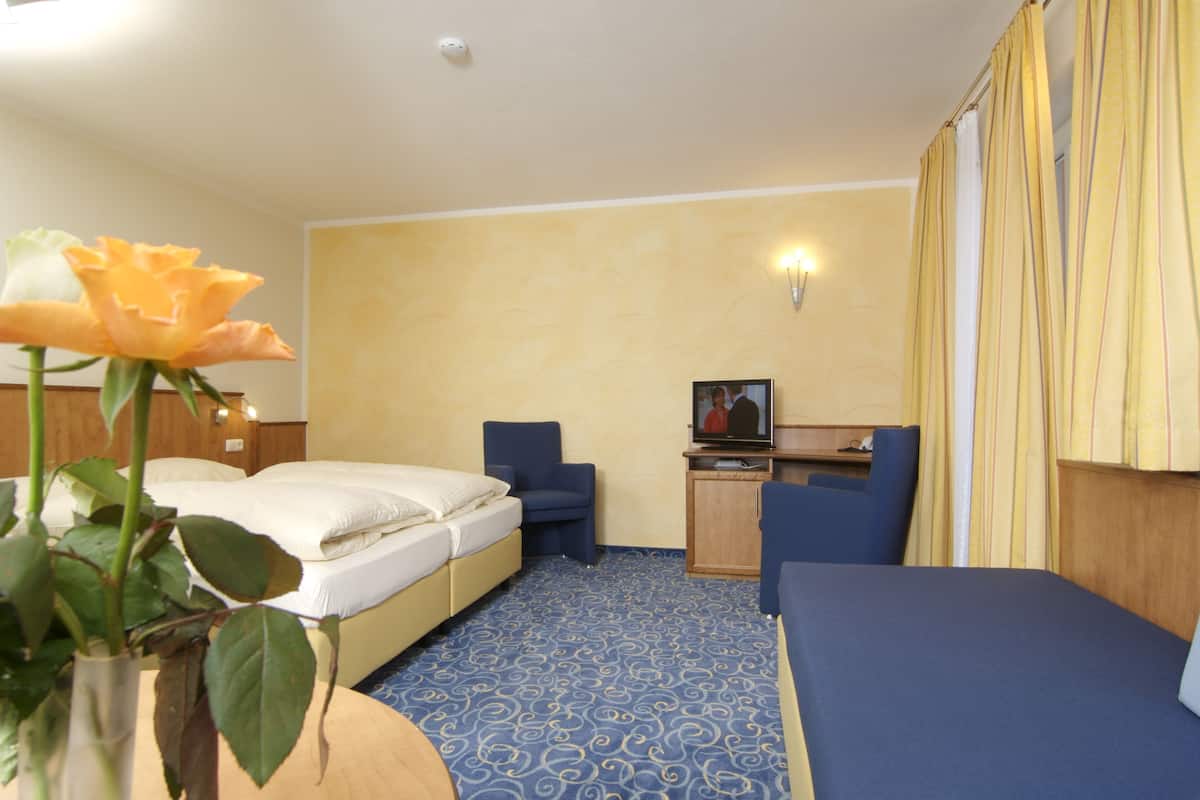 A hotel room with two beds, a desk, a TV, and a vase with a flower.