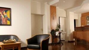 A spacious lobby with a reception desk, a black leather armchair, a wooden table with baskets, and a colorful abstract painting on the wall. - Hotel Gasthof Seefelder Hof (Dießen am Ammersee)