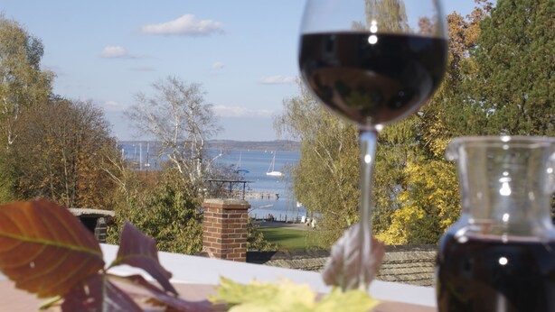 A table with a wine glass and bottle, a brick wall, and a view of a lake with boats. - Hotel Gasthof Seefelder Hof (Dießen am Ammersee)