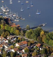 Vista aérea de uma marina com vários barcos atracados, rodeada por edifícios residenciais e um cais que se projeta na água.