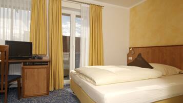 Quarto de hotel com cama, escrivaninha e televisão, e vista para o exterior através de uma janela.