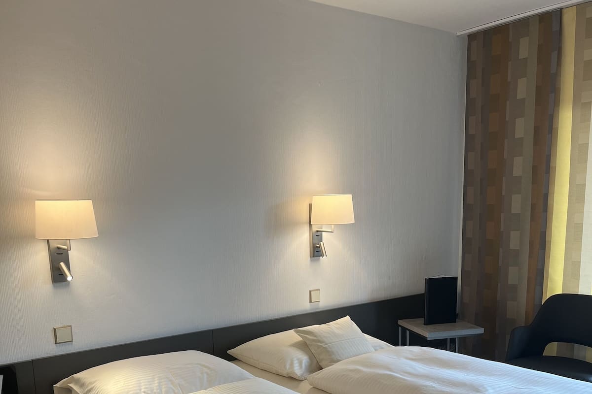 A hotel room with two beds, a nightstand, a chair, and two wall-mounted lamps.