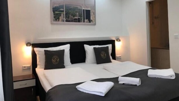Una cama doble bien hecha con ropa de cama blanca y negra, dos almohadas y una toalla doblada sobre la cama.