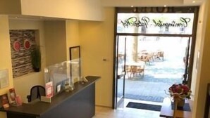 Zona de recepción con mostrador, puerta de cristal que da al exterior y vista del área de estar al aire libre.