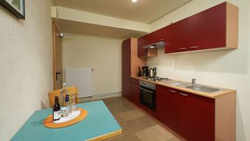 A compact kitchen with red cabinets, a wooden countertop, and a table with bottles and glasses.
