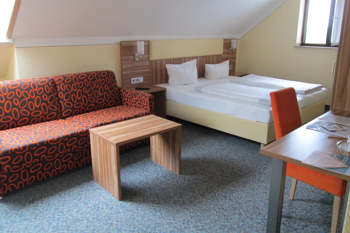 Een kleine, knusse kamer met een bed, een bank, een tafel en een stoel.